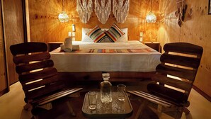 Une pièce en bois avec un lit, deux chaises, une table et des lampes fixées au mur.