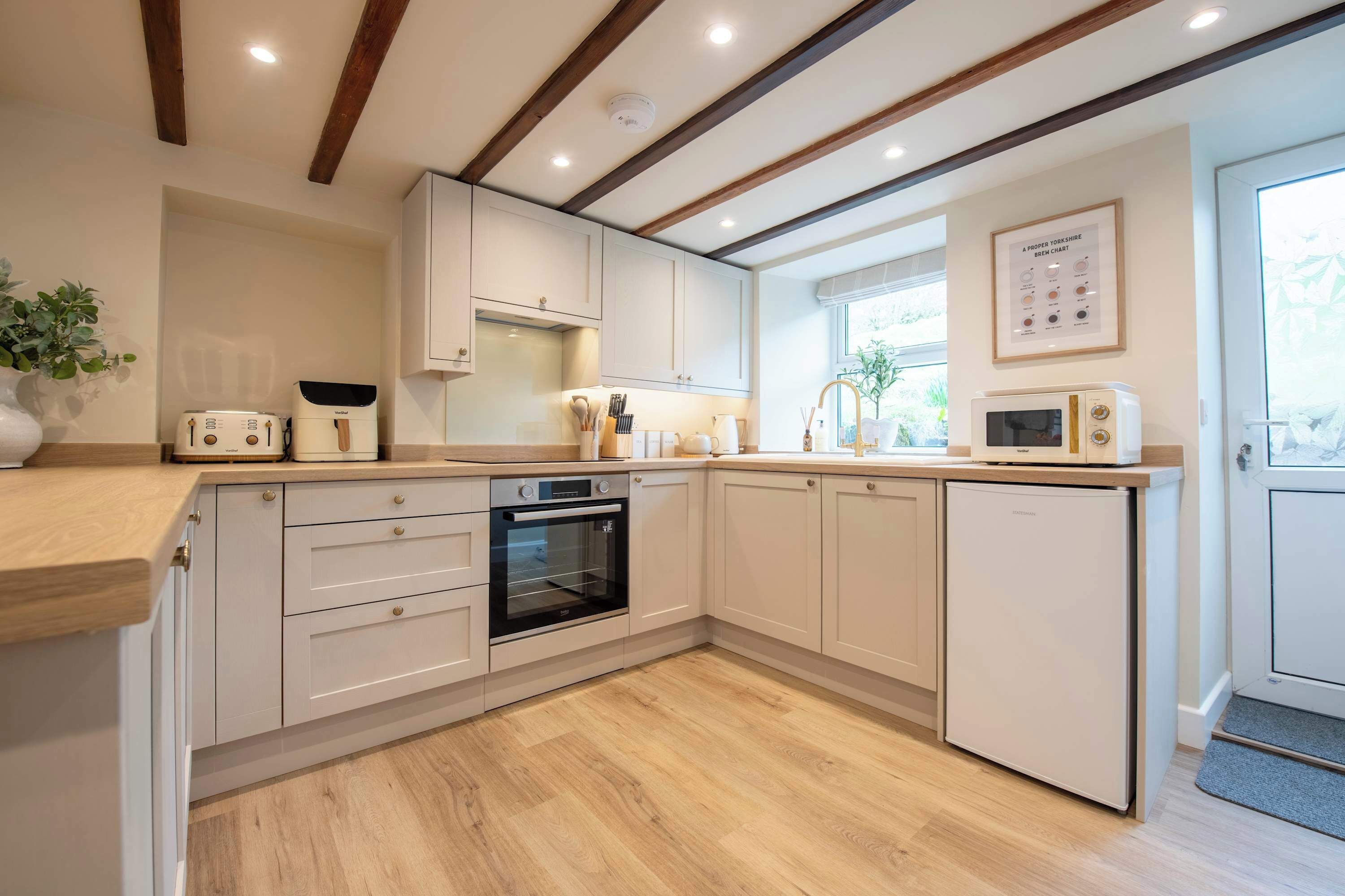 A modern kitchen with white cabinets, a built-in oven, a microwave, and a small refrigerator.