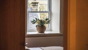 A window with a woven basket containing flowers, a radiator below, and a glimpse of a building outside.