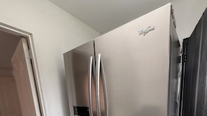 Un réfrigérateur Whirlpool en acier inoxydable dans une cuisine aux murs blancs et au sol carrelé.