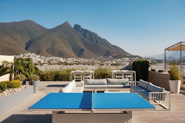 Terraza en la azotea con mesa de ping pong, mobiliario exterior y vistas a montañas y un pueblo.