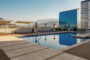 A rooftop pool with lounge chairs, a wooden deck, and a view of mountains and buildings. - Nido x Gran Ciudad Nuevo Sur (Monterrey)