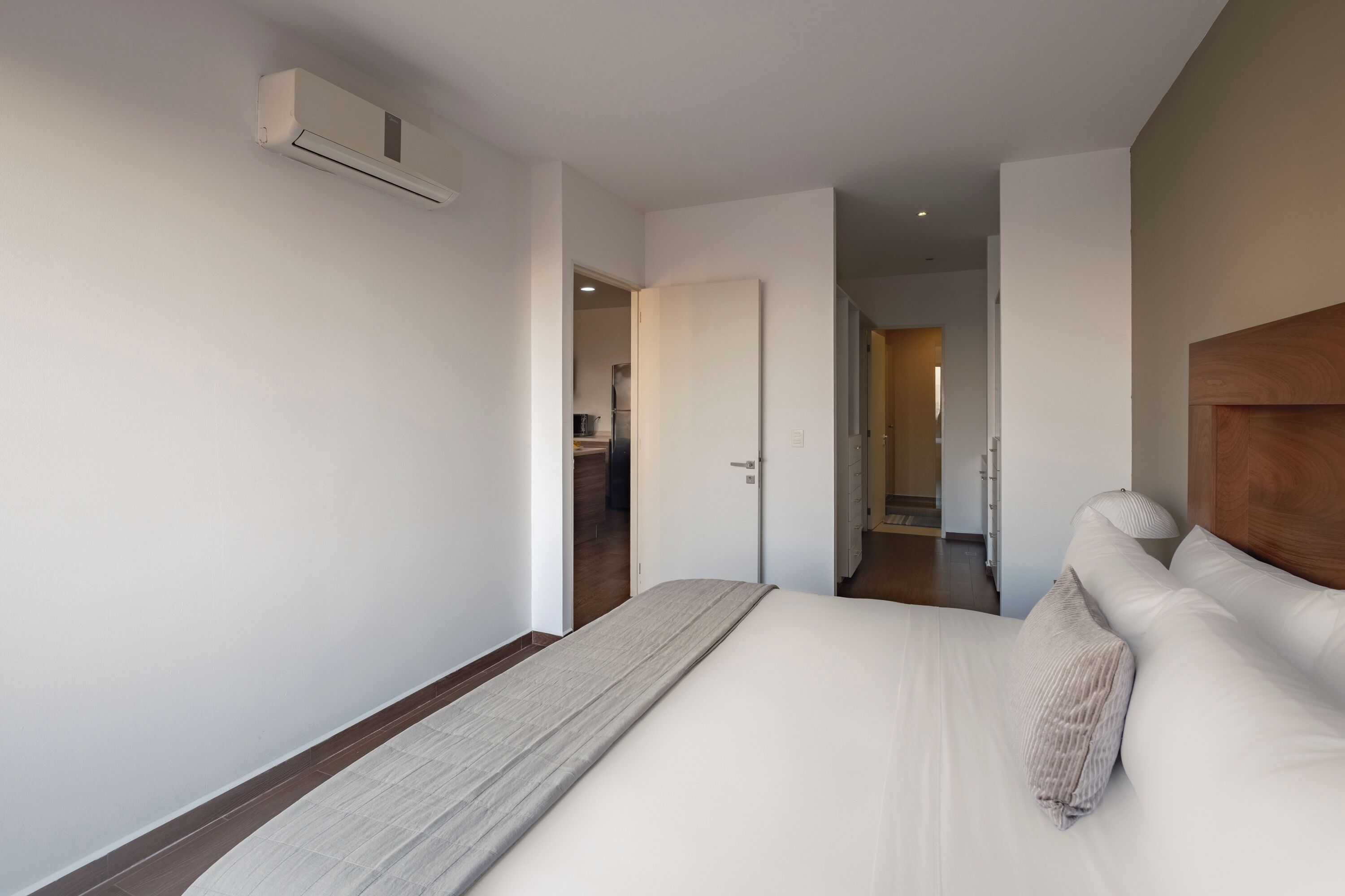 Une chambre d’hôtel moderne avec un grand lit, une tête de lit en bois et un appareil de climatisation fixé au mur.