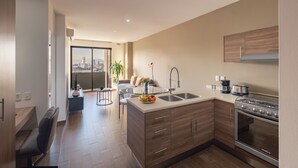 Ett modernt kök med en inbyggd spis, en matplats med ett glasbord och utsikt över en stadssiluett genom ett stort fönster.