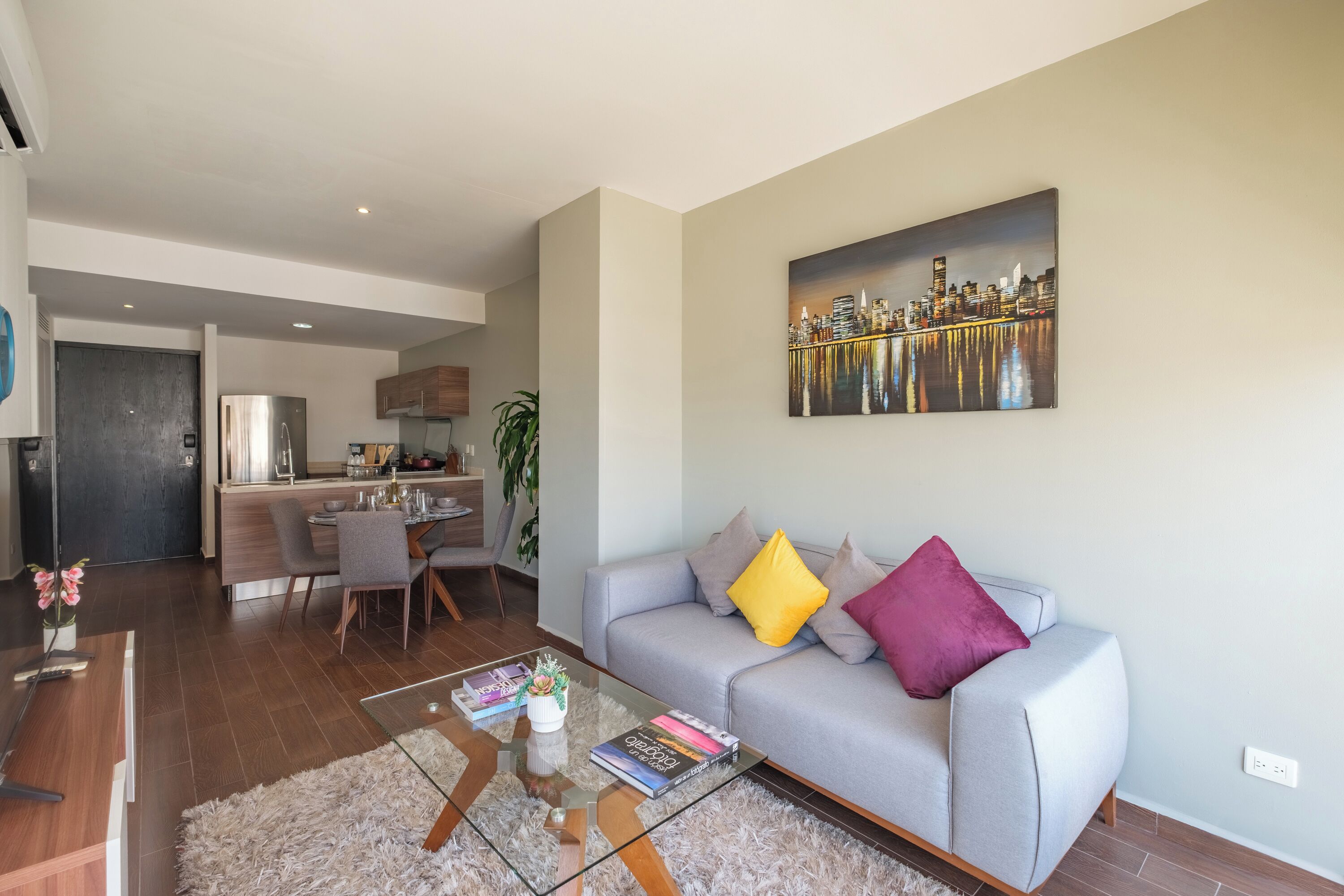 Uma sala de estar moderna com sofá, mesa de centro e uma pintura da paisagem urbana.