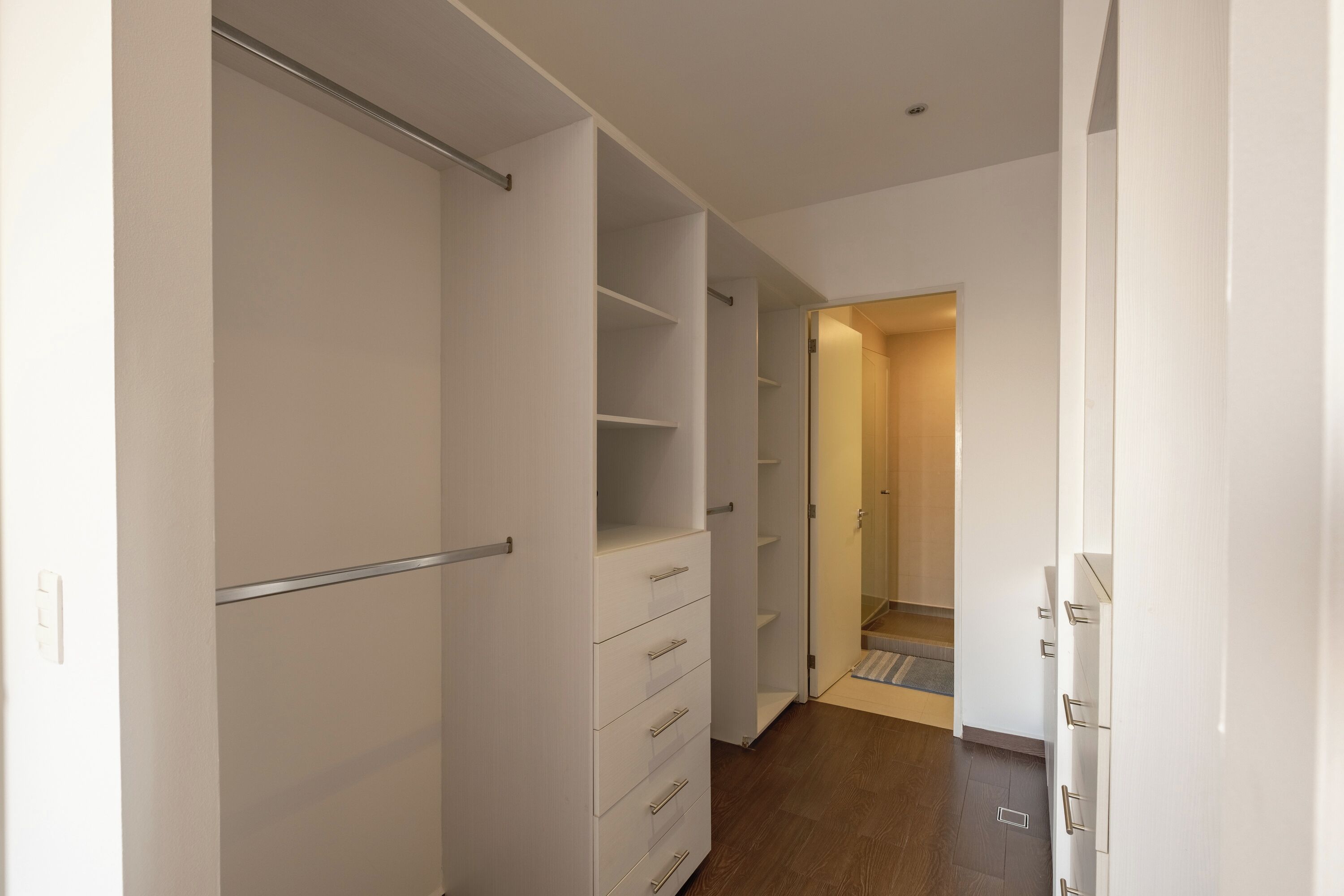A hallway with a closet, a door leading to another room, and a wooden floor.