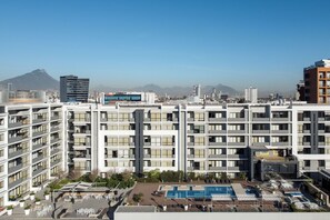 Un hotel moderno con varios pisos, una piscina en la azotea y vistas a montañas distantes.