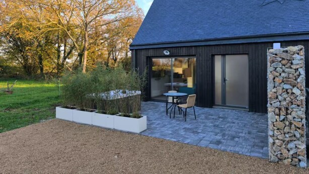Un edificio moderno con techo inclinado, un patio con mesa y sillas, y una pared de piedra.