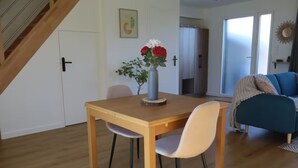 Un comedor con una mesa de madera y dos sillas, un jarrón con flores y un sofá azul al fondo.