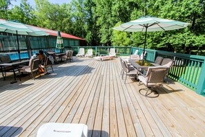 A wooden deck with outdoor seating, including chairs and tables, and a large umbrella providing shade. - 2BR Retreat nr Downtown Helen | Pool & Gym Access! (Helen)
