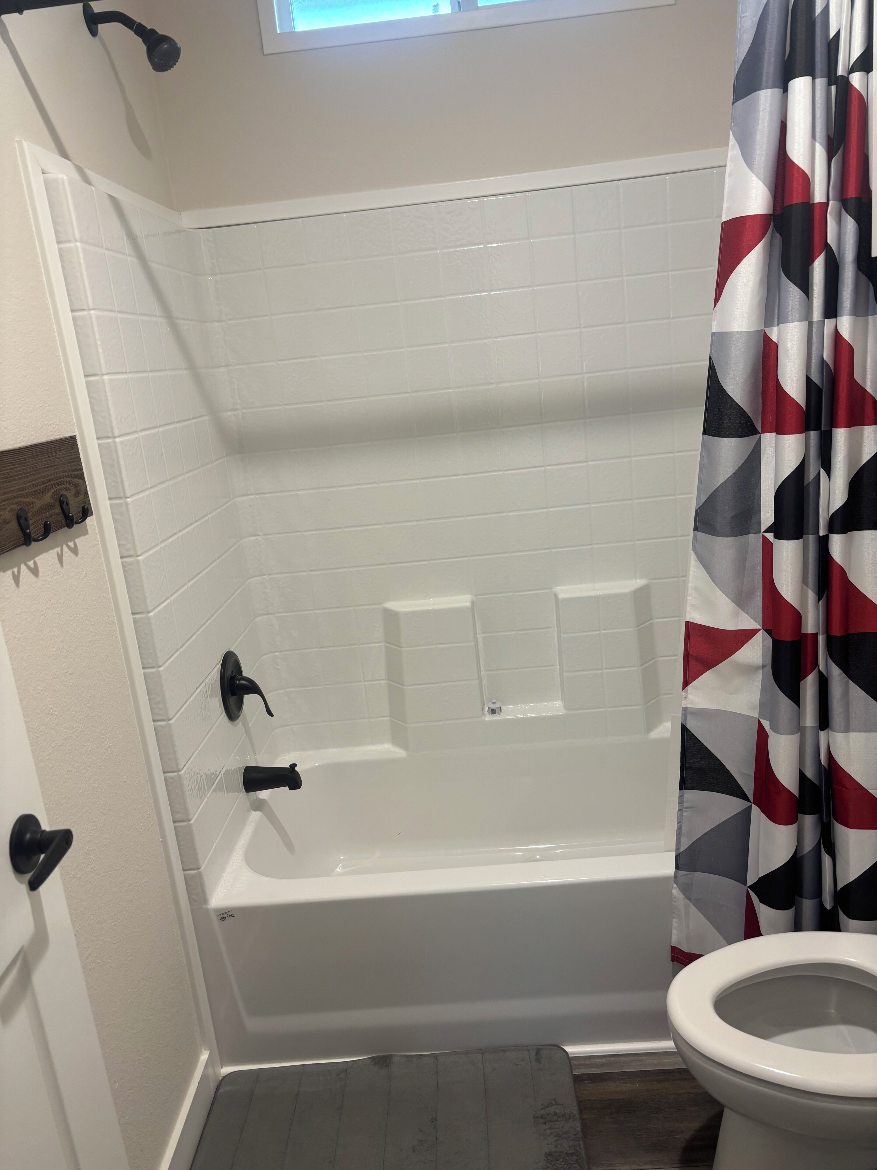 A bathroom with a white bathtub, a toilet, and a shower curtain with a geometric pattern.