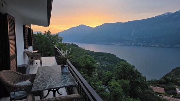 Un balcone con mobili in vimini, una pianta in vaso e vista su un lago e montagne.