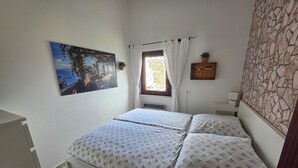 Una camera da letto con un letto, una finestra con tende e un quadro appeso al muro, con una parete a effetto pietra.