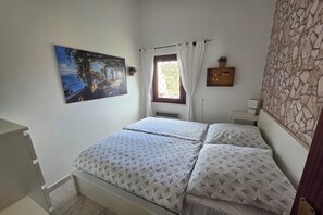 Une chambre à coucher avec un lit, une fenêtre avec des rideaux, un tableau accroché au mur et un mur dont le motif rappelle la pierre.