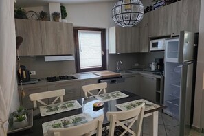 Une cuisine moderne avec des meubles en bois, une table à manger avec des chaises, un four à micro-ondes, un réfrigérateur et un luminaire suspendu.