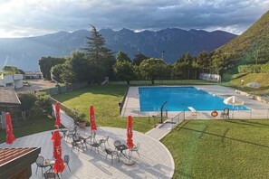 Une piscine avec une vue sur les montagnes, des espaces de détente en plein air et une zone délimitée par une clôture.