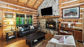 A cozy log cabin interior with a stone fireplace, a television mounted above it, and a comfortable seating area with a sofa and a couch. - Near Toccoa River • Hot Tub • Fire Pit • Gameroom - Holiday Home (Blue Ridge)