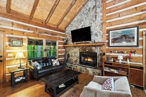 A cozy log cabin interior with a stone fireplace, a television mounted above it, and a comfortable seating area with a sofa and a couch. - Near Toccoa River • Hot Tub • Fire Pit • Gameroom - Holiday Home (Blue Ridge)