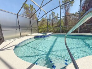 Ein Swimmingpool mit Whirlpool, umgeben von einer Glaskonstruktion mit Blick auf Bäume.