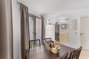 A dining area with a table, chairs, a basket of snacks, and a cabinet. - Sunset Star Holiday Home: Sea Views from Rooftop Solarium, Shared Terrace & Wi-Fi (Arguineguín)