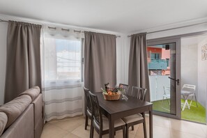 A room with a dining table, chairs, a sofa, a window with curtains, and a balcony with chairs. - Sunset Star Holiday Home: Sea Views from Rooftop Solarium, Shared Terrace & Wi-Fi (Arguineguín)