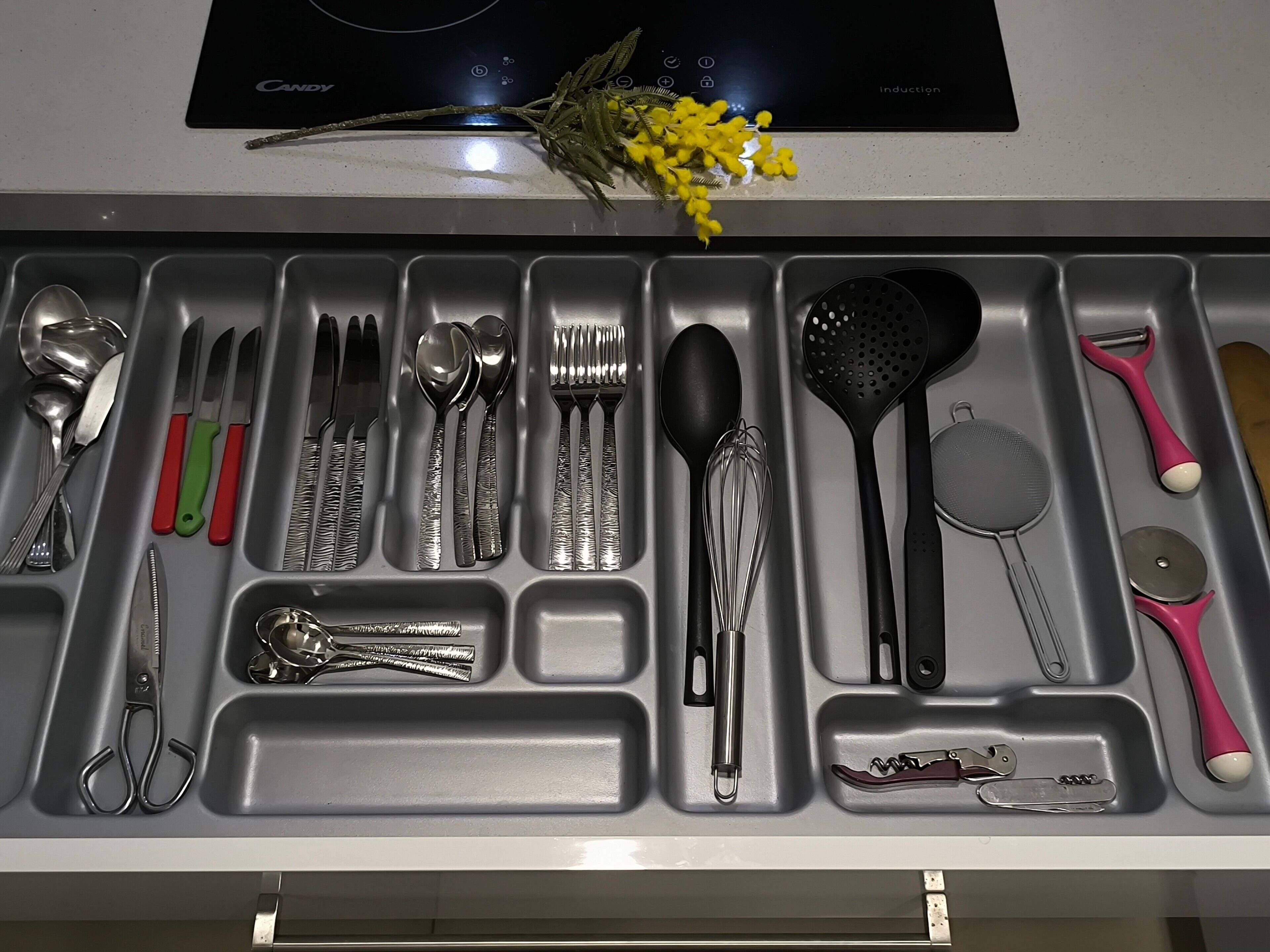 A kitchen drawer with utensils and a black induction cooktop above it.