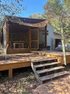 Une terrasse en bois avec des marches menant à une maison dotée de grandes fenêtres et d’un porche couvert.