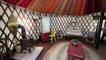 A yurt interior with a stove, a red table, a yellow chair, and a hanging chair.