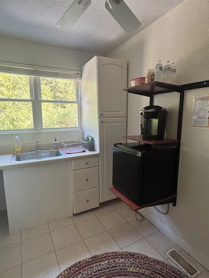 Eine kleine Küche mit Fenster, Kühlschrank, Kaffeemaschine und Spüle.