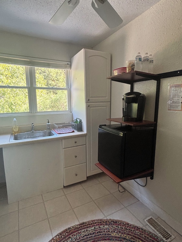A compact kitchen with a window, a refrigerator, a coffee maker, and a sink.