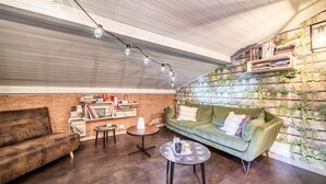 A cozy living room with a green sofa, a coffee table, a bookshelf, and a wall-mounted plant display.