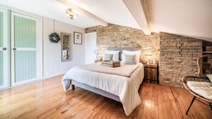 A bedroom with a bed, a stone wall, a wicker chair, and a wooden floor.