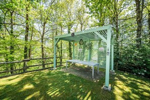 A green pergola with a bench in a wooded area.