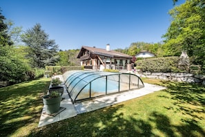 A house with a glass greenhouse structure, a well-maintained lawn, and a stone wall.