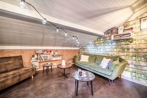 Una sala de estar acogedora con un sofá verde, una mesita de centro, una estantería y un conjunto de plantas colgadas en la pared.