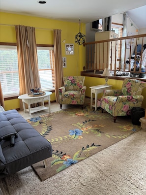 Una sala de estar con muebles de estampado floral, una alfombra con diseño y una escalera.