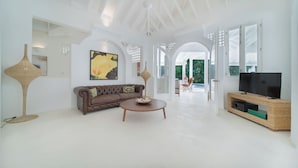 A spacious living area with a brown leather sofa, a round coffee table, a large flat-screen TV on a wooden stand, and a wicker side table. - Charming Italian Villa in Casa de Campo (Casa de Campo)