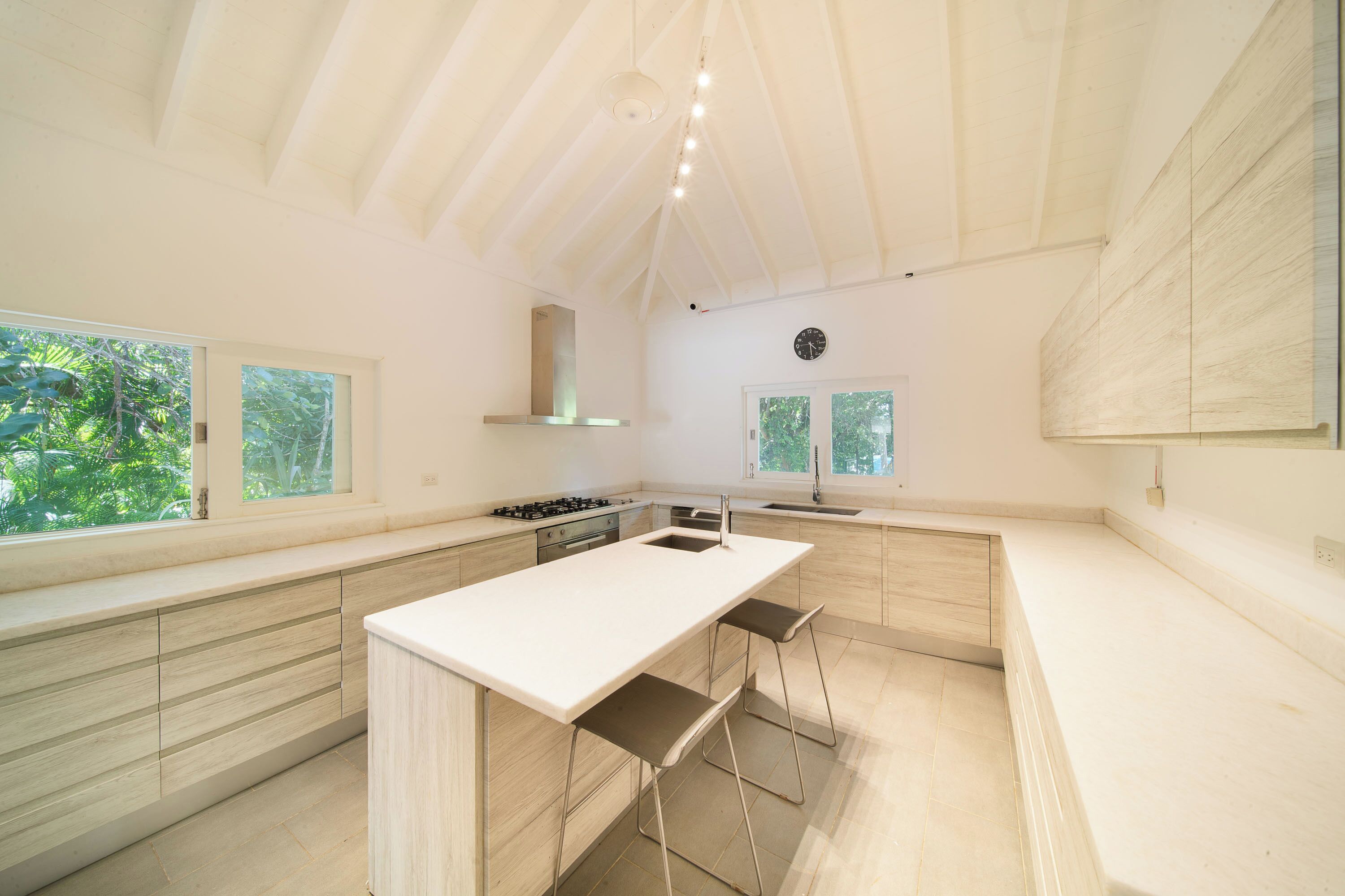 A modern kitchen with a central island, bar stools, and large windows.