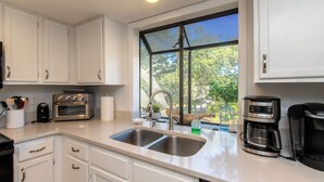A modern kitchen with white cabinets, a double sink, a toaster, a coffee maker, and a window with a view of trees. - 764 Summerwind Villa | Peaceful Edisto Escape | Golf, Lagoon & Wildlife Views | Easy Beach Access (Edisto Beach)