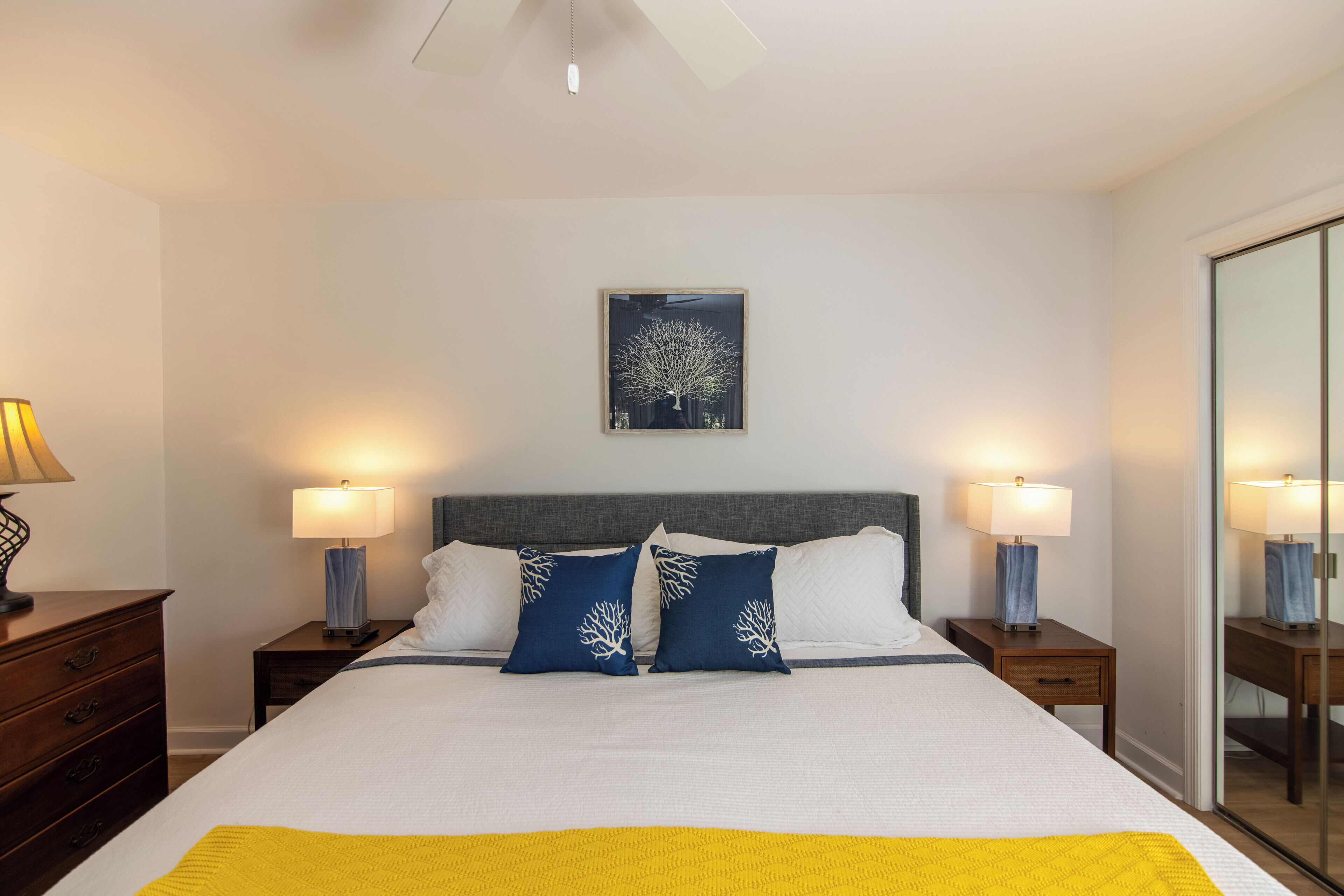 Una camera d'albergo ordinata con un letto grande, due comodini con lampade, un'opera d'arte appesa al muro e uno specchio sulla parete destra.