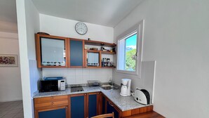 Cuina compacta amb armaris de fusta, microones, cafetera i finestra amb vista a vegetació.