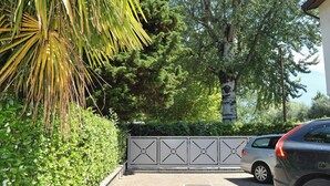 Un carrer amb tanca que condueix a un cotxe aparcat, envoltat de vegetació i arbres exuberants.
