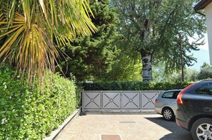 A gated driveway leading to a parked car, surrounded by lush greenery and trees. - Modern beachfront apartment "Lago Blu" right on the lake (Riva del Garda)