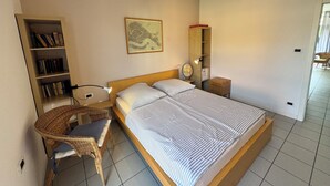 Un dormitori amb un llit, una cadira, una estanteria, un mapa a la paret i una taula petita.