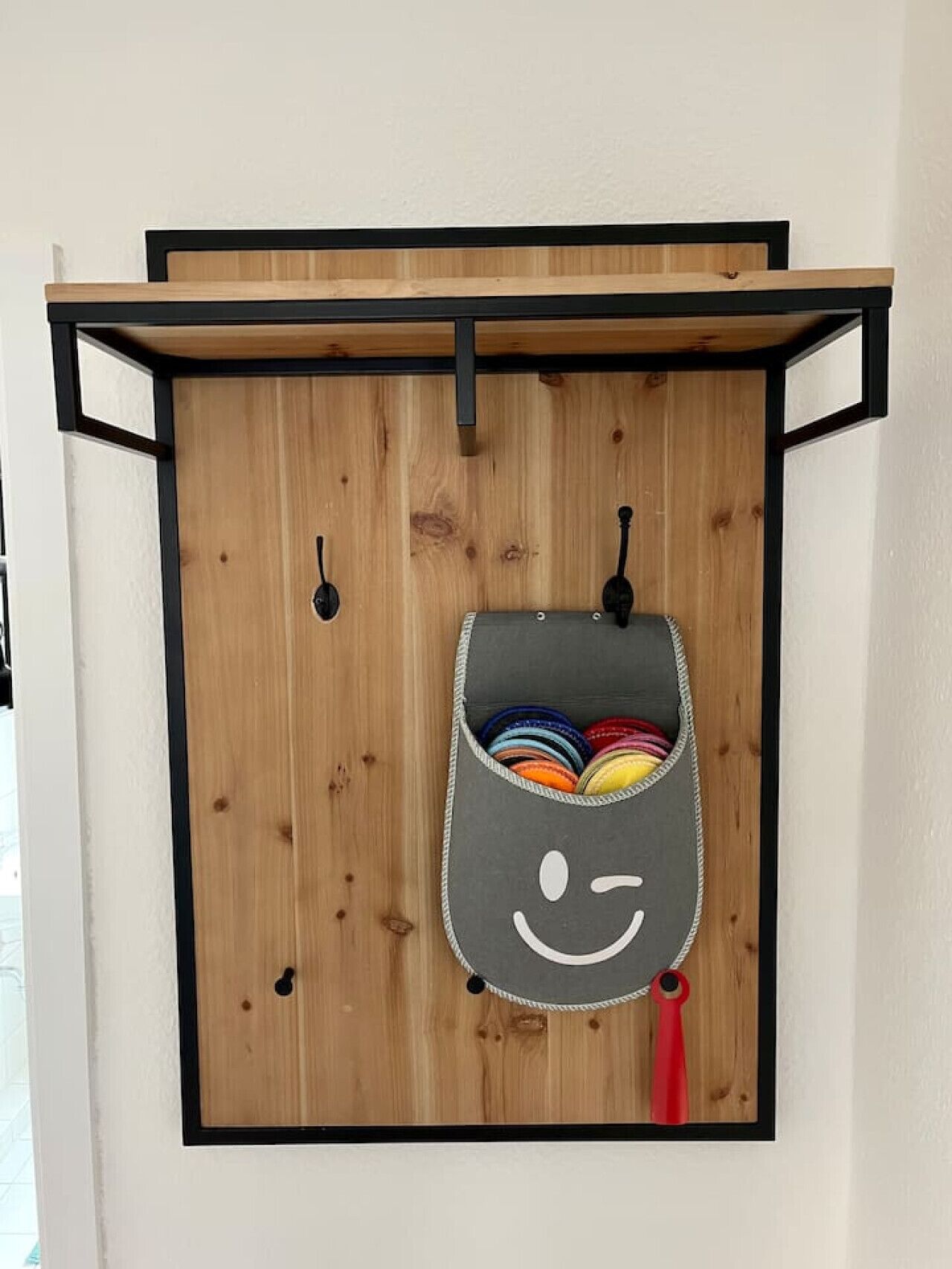 A wooden wall with a gray bag hanging from a black metal bracket, containing colorful items.