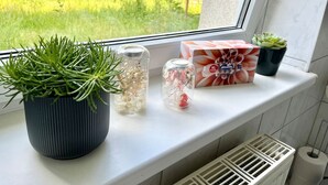 Un rebord de fenêtre orné d’un pot de plante, de deux bocaux en verre contenant des fleurs séchées, d’une boîte de thé Alouette et d’une petite plante succulente.