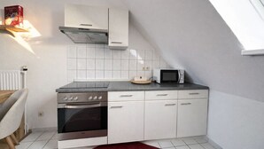 Een compacte keuken met witte kastjes, een inbouwoven, een magnetron en een raam boven de gootsteen.