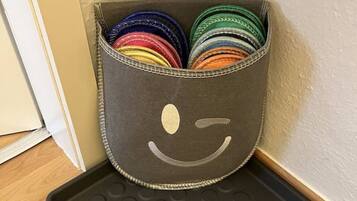 A corner storage basket with a smiley face design, containing various colorful items.
