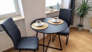 Un petit coin repas avec une table ronde et deux chaises, chacune agrémentée d’une tasse de café posée sur un set de table en fibres tressées.