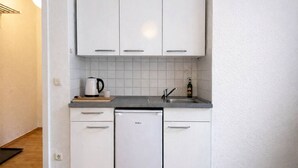Une cuisine de taille réduite, avec des meubles blancs, un lave-vaisselle, une machine à café et un évier.